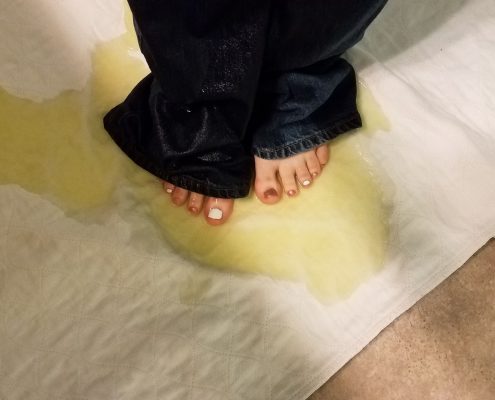 Sosha's bare feet standing in her pee puddle, still wearing her wet pants.