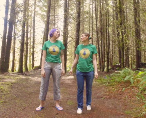 Oliva and Sosha both look at each other as they stand in the forest in their soaked pants.