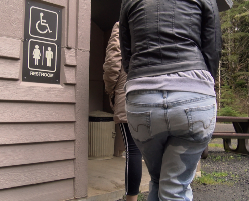 A woman wets her pants while waiting in line for a public toilet.